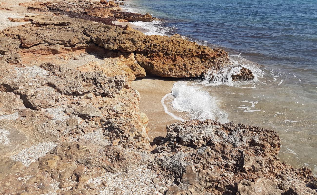 Photo de Cala l'Arjub avec sable brun avec roches de surface